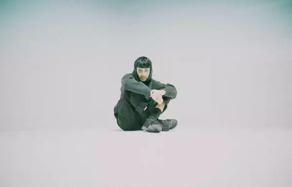 Factory Sounds 2023 cohort member Rohaan sits in an empty space wearing a grey tracksuit and trainers