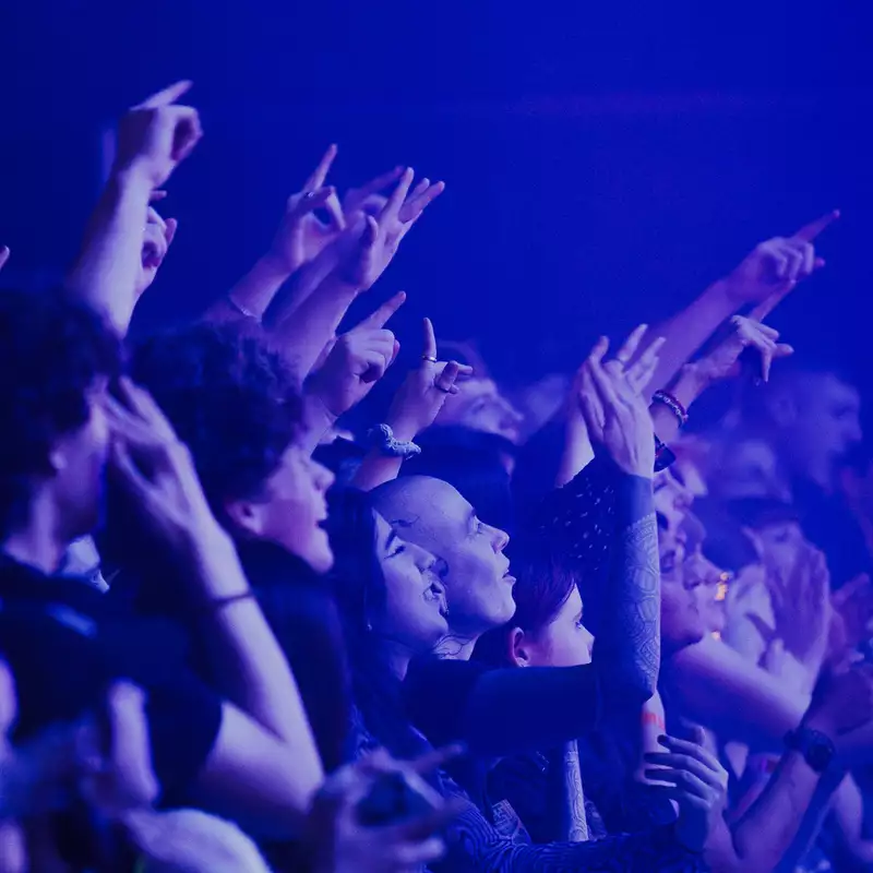 A crowd of people cheering and filming over the barrier in the Warehouse at Aviva Studios. The lighting is blue.