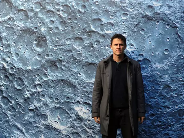 Luke Jerram, a male artist stood in front of a close up of a moon crater artwork