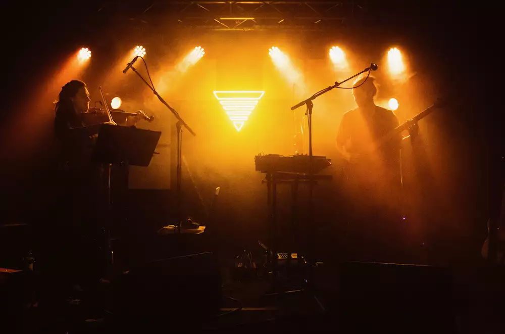 Two members of Manchester Collective performing on a stage with hazy yellow lighting