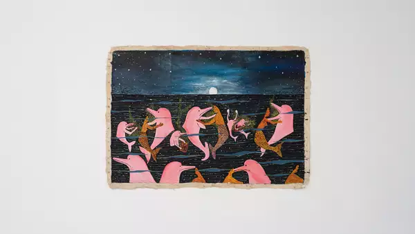 An artwork by Santiago Yahuarcani, showing dolphins and mermaids. The artwork is displayed on a white wall.