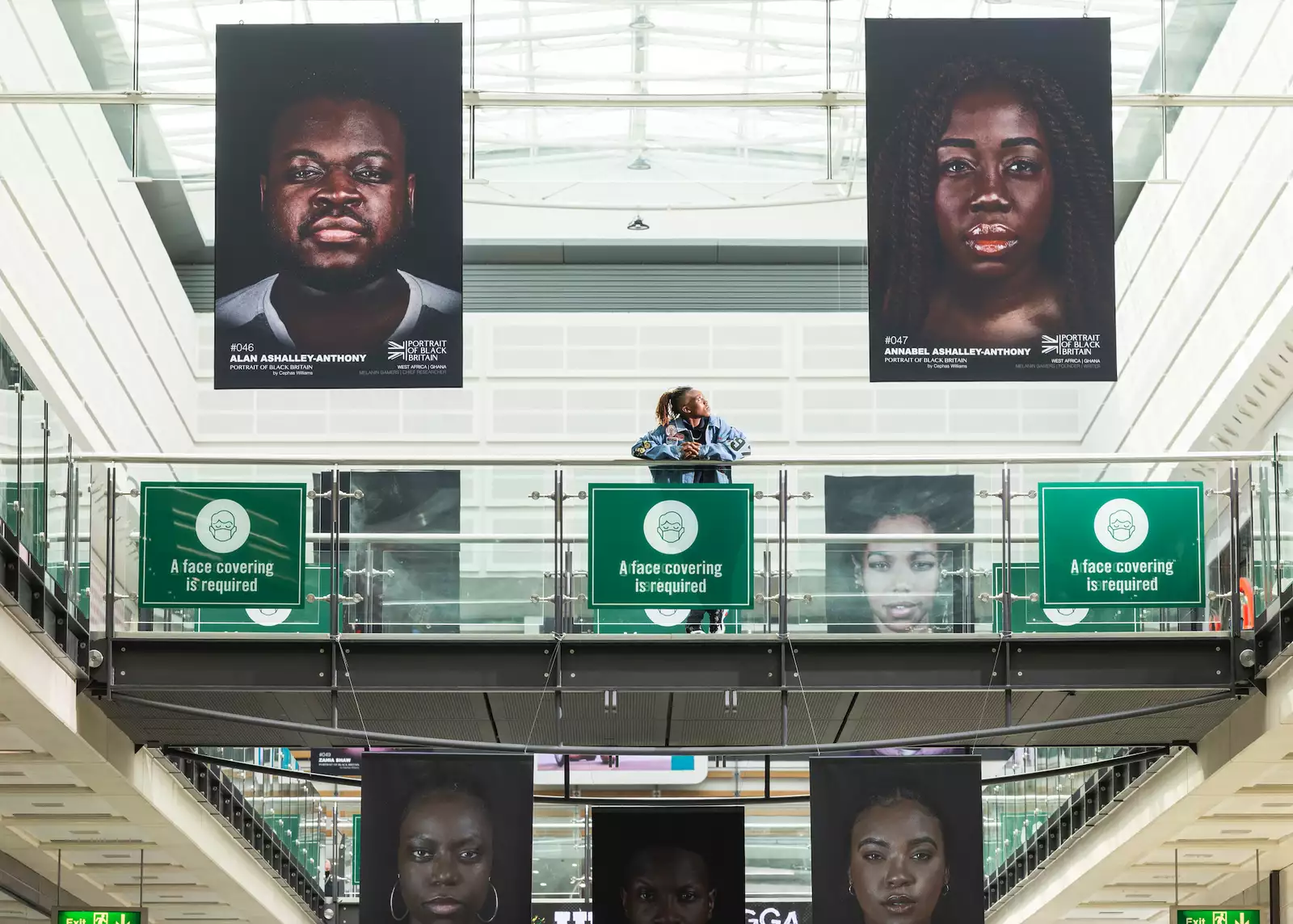 Photo of person looking at large banners of images from Portraits of Black Britain hanging from ceiling in the Arndale Centre